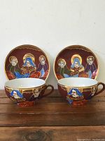 Front view of two hand painted traditional Japanese Satsuma tea cups paired with matching saucers showing detailed artwork and gold leaf accents.