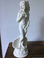 Front view of white alabaster statue showing nude female figure with clam shell behind her and floral base.