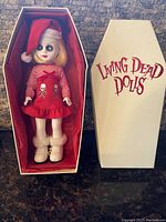 Living Dead Doll "NoHell" 10 inch doll inside original coffin-shaped box with lid removed, doll dressed in red and white holiday themed outfit, with skull motifs, white boots and Santa hat.