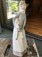Front view of Lladró porcelain figurine showing girl with goat in arms on rustic wooden surface near door.