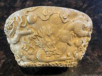 Exterior of carved oriental bowl showing detailed dragon and cloud motifs in relief.