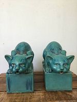 Front view of pair of turquoise glazed ceramic cat statues on rectangular bases, showing facial details and glaze variation