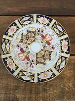 Top view of Royal Crown Derby tea plate showing intricate floral and geometric pattern in gold, navy blue, red on white porcelain.