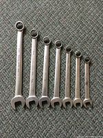 Seven combination wrenches of varying sizes laid out on carpeted surface showing both open and box ends.