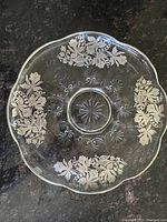 Top-down image of the clear glass pedestal platter showing silver overlay daffodil floral patterns in four sections around the edge and embossed floral and starburst details at the base center.