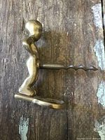 Photo showing side profile of brass human figurine corkscrew lying on wooden surface