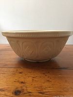 Side view of the beige/cream ceramic bowl showing the embossed cloverleaf pattern around the exterior sides and ribbed rim edge.