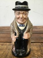 Front view of Winston Churchill ceramic toby jug showing detailed facial features, bow tie, umbrella, and trench coat