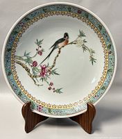 Front-facing view of round dish on wooden stand, showing full bird and blossom motif with gilt border