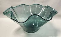 Side angle view of the scalloped blown glass bowl showing the fluid and wavy rim and translucent green-blue color.