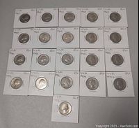 21 silver USA Washington quarters arranged on a flat surface in individual white holders with handwritten dates and notes