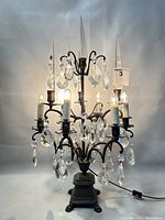 Front view of antique bronze 6-arm table lamp illuminated with lit bulbs, displaying crystal pendants and claw feet base