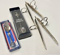 Photo showing two silver plated asparagus tongs alongside two boxed sterling spoons labeled Iona Abbey and one commemorating Queen Elizabeth II