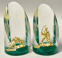 Front view of the pair of slanted Lucite paperweights with gold-toned figurines inside.