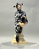 Front view of Royal Doulton porcelain Jester figurine in black and white costume seated on a pedestal.