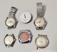 Front view of 6 vintage men's mechanical watches and a loose dial showing different dial and case styles.