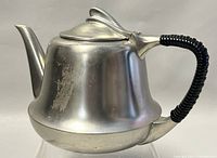 Side view of Art Deco pewter teapot showing handle, body, and lid with surface wear.