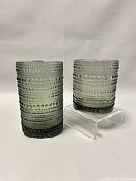 Front view of two smoked glass tumblers, one taller 5 inch and one shorter 3.5 inch, both featuring the raised bead pattern characteristic of Kastehelmi series.