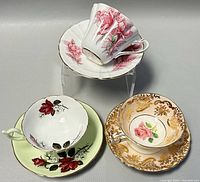 Three porcelain teacup and saucer sets with floral designs and gold trim arranged on a neutral surface.