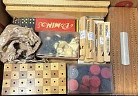 Overview of wooden and plastic game pieces, wooden game boards, Boise branded wooden whistles in packaging, and fabric bag with game pieces