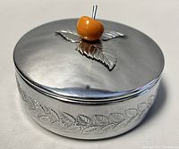Front angle of vintage Chase USA round trinket box with embossed leaf details and orange Bakelite handle on lid