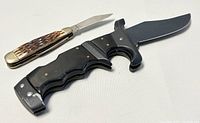 Photo showing both the large black-handled knife and small folding pocket knife side by side on a white background.
