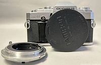 Front view of Olympus OM30 camera body with lens cap and separate lens mount adapter in front