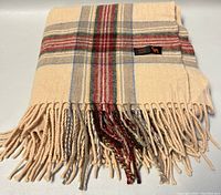 Folded view showing plaid pattern, color, and fringe tassels with brand label visible.