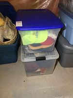 Two stacked plastic totes filled with assorted ball caps