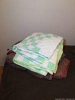 Folded green and white patchwork quilt on top of several blankets