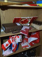 Contents of wooden shelves showing Canadian flags, brown carrying case, light-up maple leaf display, and other items as described.
