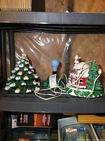 Full view of two ceramic light-up Christmas trees and the snowman scene on a shelf with cords visible