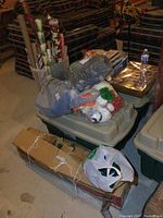 Photo of two large plastic totes with various Christmas decorations inside, including gift wrap rolls and bags of smaller items.