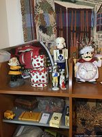 Shelf display showing ceramic chef clock, Toronto Maple Leafs nutcracker, ceramic figurines, strawberry lunch pails, and Rolling Stones poster.