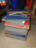 Stack of foam floor tile packages with 4 tiles each, mostly sealed, showing colorful interlocking edges and different colors of foam tile faces.