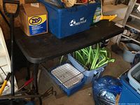 Black resin folding table with various items placed on top and under it in a garage setting.