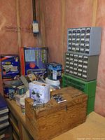 Photo showing wood toolbox on workbench with many boxed hardware items and two hardware organizers in the background.
