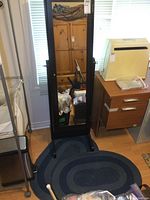 Full view of the free standing mirror with dark wooden frame and reflective glass, showing surrounding room detail.