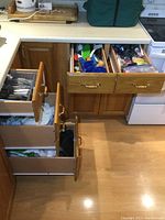 Full view of five kitchen drawers open showing cutlery, utensils, towels, and kitchen tools inside.