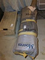 Rolled mattress topper packaged in plastic labeled Moores, showing packaging and surrounding items.