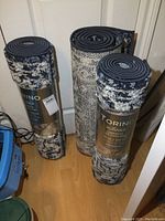 Three rolled carpet runners standing against white door on wooden floor, bundled with product labels.