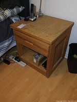 Photo of one solid wood nightstand showing rectangular top, drawer, and open shelf, with items on top and around it.