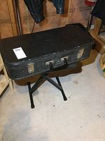 Black hard shell saxophone case closed and resting on folding music bench