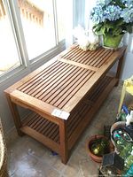 Full view of vintage teak coffee table next to window, showing slatted wood top and bottom shelf.