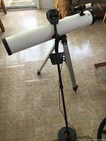 View of white reflector telescope on aluminum tripod alongside black metal detector with circular coil resting against tripod