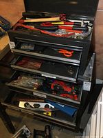 Toolboxes with drawers open showing assorted hand tools inside including bolt cutters and hatchets on top.