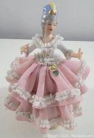 Front view of lace lady figurine in pink lace dress with white trim and blue hat
