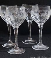 Four clear crystal claret goblets with leaf and floral engraving, displayed on a black background.