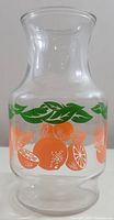 Front view of the clear glass juice carafe with orange citrus and green leaf decorations.