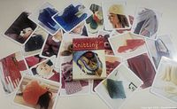 Photo showing the 'Knitting to Go' original box surrounded by 25 pattern cards illustrated with colorful knitwear images including hats, scarves, sweaters, and baby items.